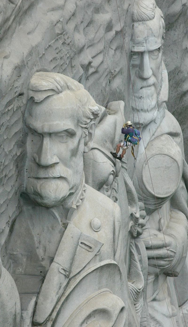 A climber dangles between the granite carvings of General Robert E. Lee (left) and General Stonewall Jackson as he rappels across the memorial. AJC file photo, 2002.