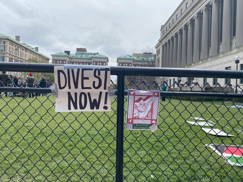 Protesters have hung signs on the gates outside of South Lawn at Columbia University, as well as inside the new encampment, demanding the school divest from companies with ties to Israel. (Alice Tecotzky for The Atlanta Journal-Constitution)