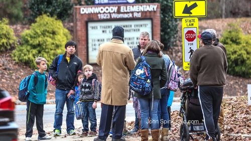 A school official converses with Dunwoody Elementary School parents and students on the corner of Womack Road and Lakeland Woods Court.