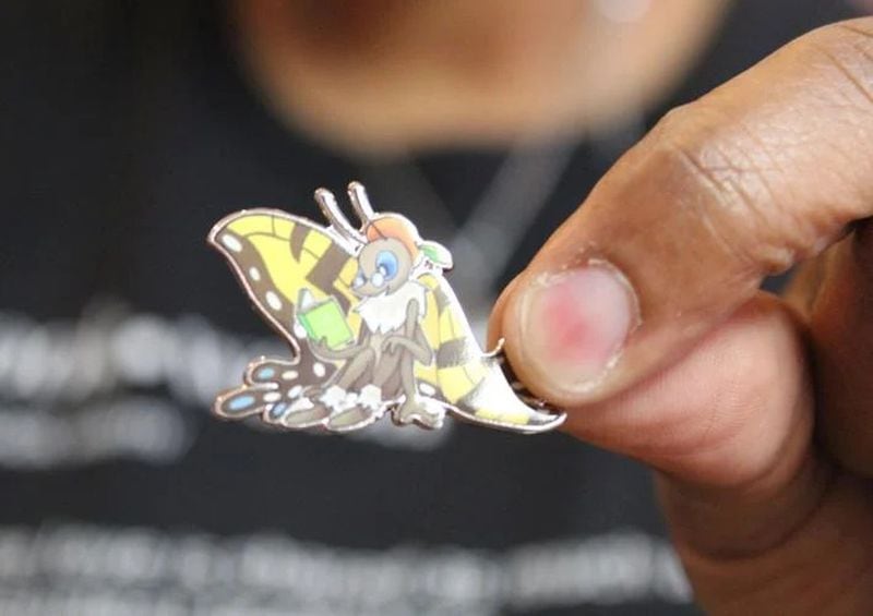 Julia Davis, owner of the Book Worm, holds up a pin of Paige Turner, the mascot of Book Fest. These pins will be given out at the festival next Saturday. (Photo Courtesy of Joe Adgie)