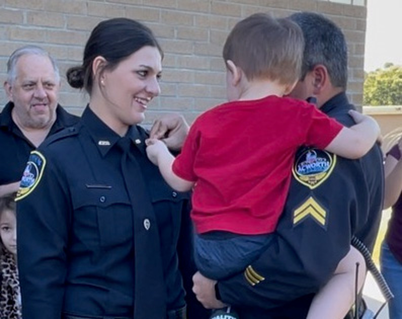 Michelle Mistretta has her police badge pinned on by her brother, Eric Mistretta, and her son.