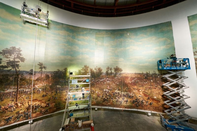 Conservators on scissor lifts complete the restoration of “The Battle of Atlanta,” including adding back one of the vertical sections that was missing, seen at right. Artisans used chopsticks wrapped with cotton bolls to clean the mammoth painting. CONTRIBUTED: ATLANTA HISTORY CENTER
