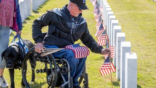 Don Dowling places flags in front of tombstones at the Georgia National Cemetery in Canton on Saturday. Volunteers will place an estimated 21,000 flags on tombstones during the ceremony.