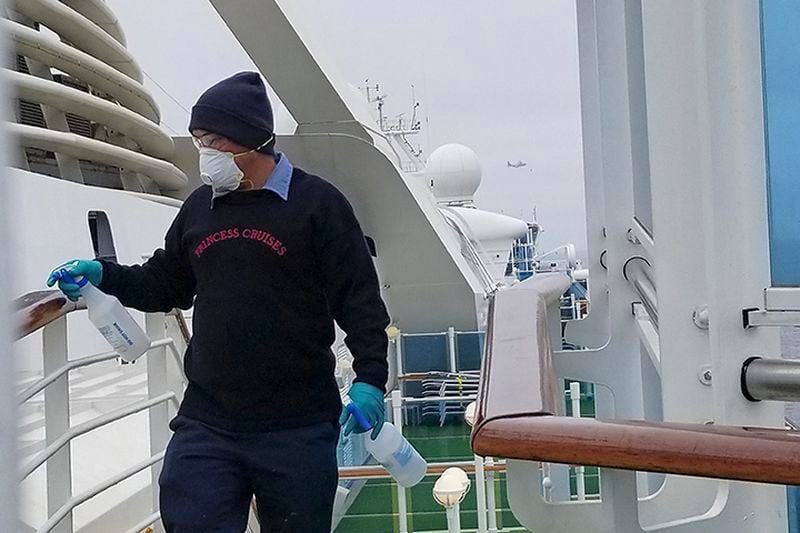 A cruise ship worker cleans a railing on the Grand Princess Thursday off the California coast. Princess Cruise Lines said fewer than 100 people aboard had been identified for testing.