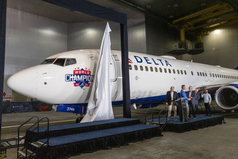 People watch a curtain fall that reveals the Delta Air Lines jet dedicated to the Braves World Series championship Thursday, July 28, 2022. (Steve Schaefer / steve.schaefer@ajc.com)