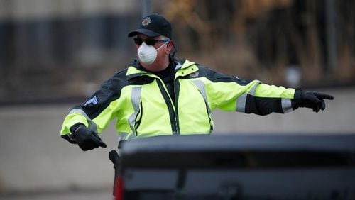 A Denver Police Department officer wears a surgical mask while directing traffic at a coronavirus drive-thru testing site outside the Denver Coliseum Saturday, March 14, 2020, in Denver. (AP Photo/David Zalubowski)