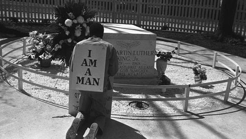 A striking Atlanta sanitation worker kneels at the grave of Dr. Martin Luther King Jr. after a rally by Southern Christian Leadership Conference supporting the strike in Atlanta on April 4, 1970. King was killed in Memphis, Tenn., two years earlier while supporting a sanitation workers’ strike there. The picket signs reading “I Am A Man” were first used in the Memphis strike. (AP Photo/BJ)