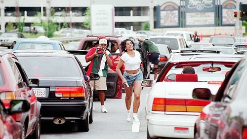 A woman runs back to her car after posing quickly for another Freaknik participant near Phipps Plaza and Lenox Mal.l After the malls closed traffic came to a standstill on Peachtree and Lenox Roads during the 1995 gathering. AJC FILE