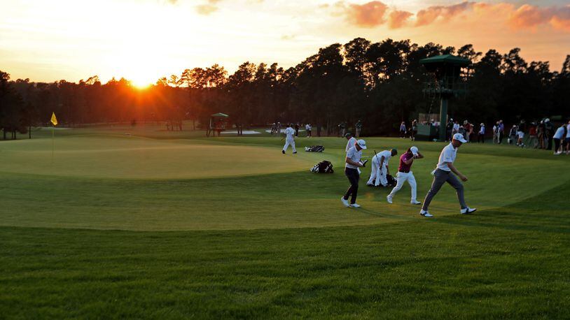 The final group of Cameron Smith, center, Abraham Ancer, and Justin Thomas walk off of the 18th green at sun set during the third round of the Masters Saturday at Augusta National. (Curtis Compton / Curtis.Compton@ajc.com)