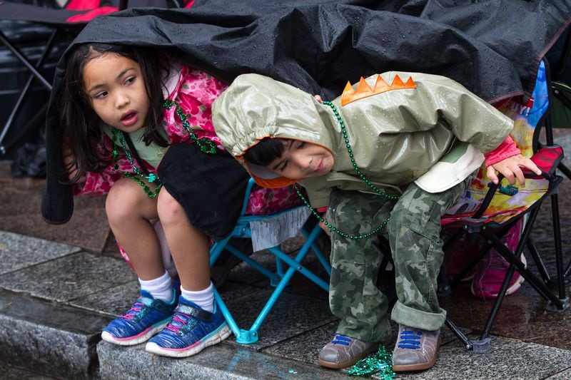 Varona Malkoff (left) and her brother Drexel try to stay dry while watching the  St. Patrick's Parade in  Atlanta on Peachtree Street on Saturday, March 17, 2018. STEVE SCHAEFER / SPECIAL TO THE AJC