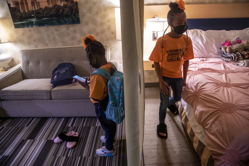 A curtain separates the living room from the bedroom as Runyia McKiver, 10, right, makes the bed she shares with her little sister, Brooklyn Mitchell, left, in their hotel room at Home2 Suites in Newnan. Runyia says she likes being a big sister because she likes to teach her sister Brooklyn new things. (Alyssa Pointer / Alyssa.Pointer@ajc.com)