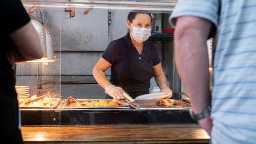 Marie Rodriguez helps a customer from behind acrylic panels during the lunch rush at Matthews Cafeteria on Main Street in Tucker on July 17, 2020. The dining institution, established in 1955, ask customers to wear masks, added the acrylic dividers, made separate entrance and exit doors and have drive-up service.