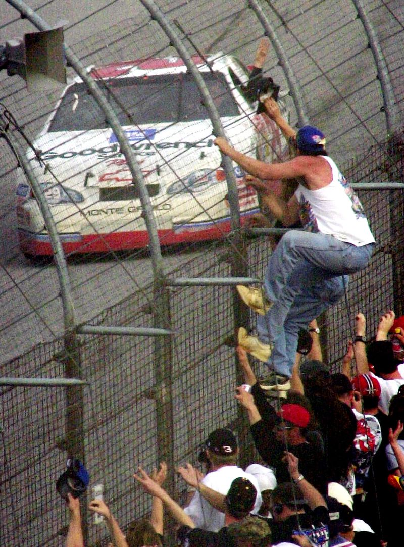 Fans climb the fence as Kevin Harvick holds up three fingers in honor of Dale Earnhardt Sr. as he drives by in the GM Goodwrench Chevrolet after winning the NASCAR Cracker Barrel 500 at Atlanta Motor Speedway, Sunday, March 11, 2001. Harvick was driving for the team in place of Earnhardt, who was killed in a crash at Daytona. (AP Photo/Joe Sebo)