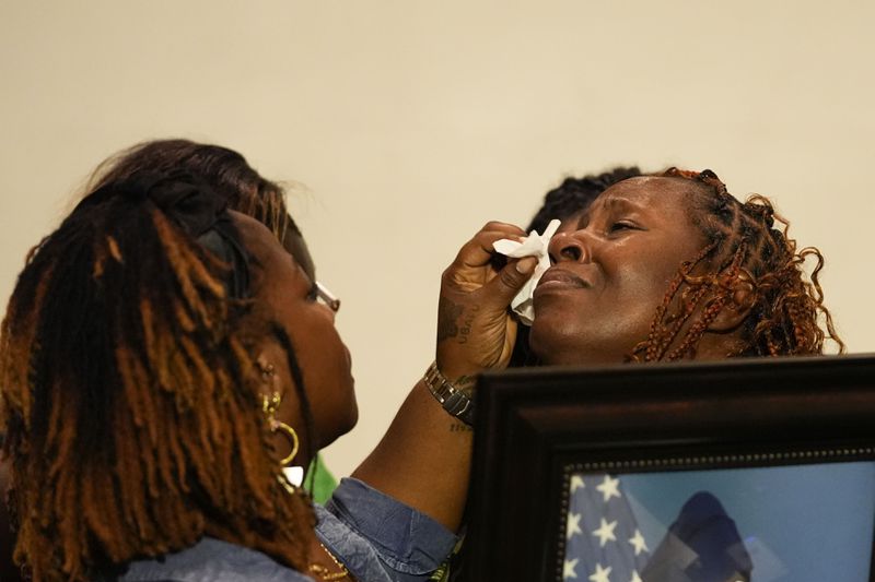 Family members wipe away the tears of Chantimekki Fortson, mother of Roger Fortson, a U.S. Navy airman, as she holds a photo of her son during a news conference regarding his death, with Attorney Ben Crump, Thursday, May 9, 2024, in Ft. Walton Beach, Fla. Fortson was shot and killed by police in his apartment on May 3, 2024. (AP Photo/Gerald Herbert)