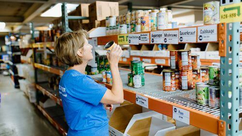 A volunteer at North Fulton Community Charities at the food pantry removing a can of food from a very bare shelf to fill a family’s food request. (Courtesy North Fulton Community Charities)