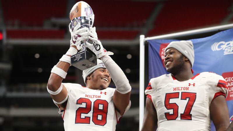  Milton defensive back Joseph Charleston (28) celebrates with the state championship trophy next to lineman Paul Tchio (57) after their 14-13 win over Colquitt County in the Class AAAAAAA State Championship at Mercedes-Benz Stadium. (Jason Getz/Special to the AJC)