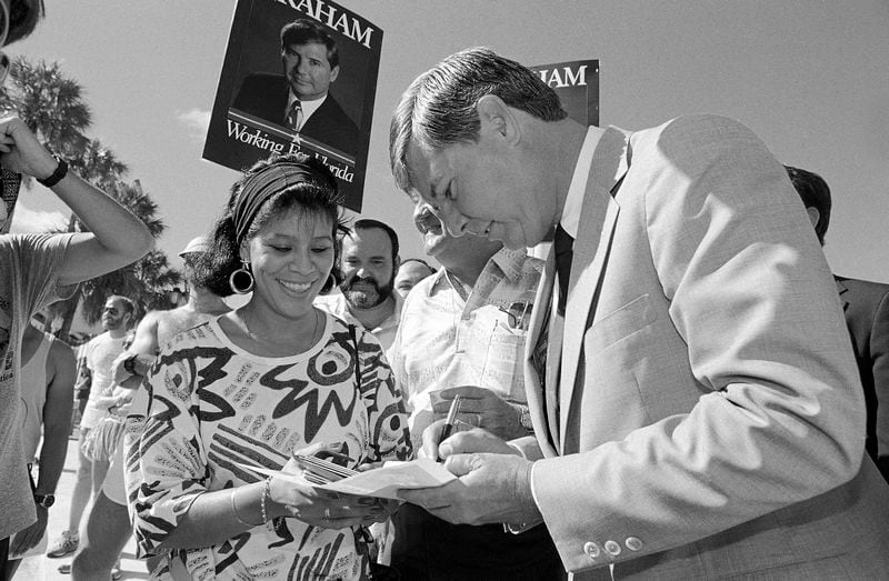 FILE - Florida Gov. Bob Graham, right, signs an autograph for Maria Dulce before a campaign appearance at the Miami River Festival in Jean Marti Park, Oct. 25, 1986, in Miami. Graham, who chaired the Intelligence Committee following the 2001 terrorist attacks and opposed the Iraq invasion, has died, according to an announcement by his family Tuesday, April 16, 2024. (AP Photo/Kathy Willens, File)