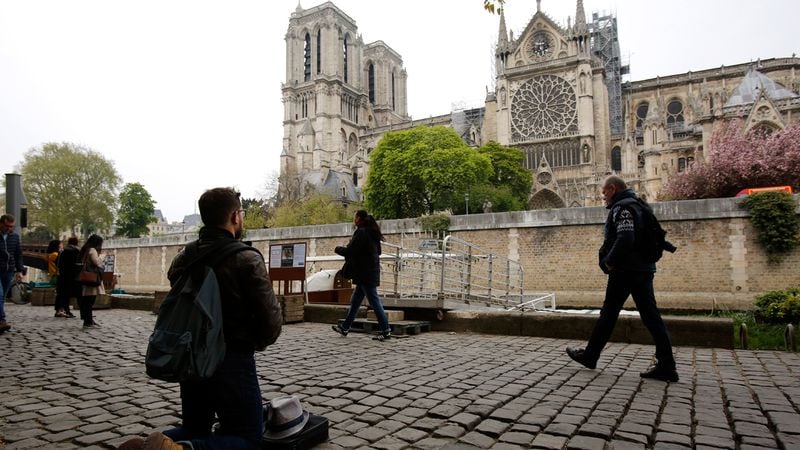 Man kneels as people came to watch and photograph the Notre Dame cathedral after the fire in Paris, Tuesday, April 16, 2019. Experts are assessing the blackened shell of Paris' iconic Notre Dame cathedral to establish next steps to save what remains after a devastating fire destroyed much of the almost 900-year-old building. With the fire that broke out Monday evening and quickly consumed the cathedral now under control, attention is turning to ensuring the structural integrity of the remaining building.