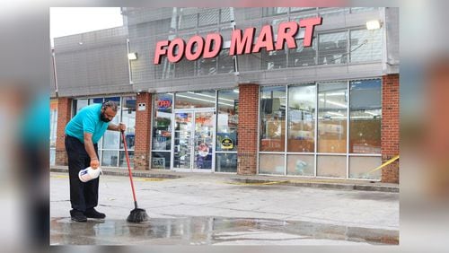 Food Mart owner Kuldip Rakkar pours bleach on a pool of blood following a shooting outside the Old National Highway business Tuesday.