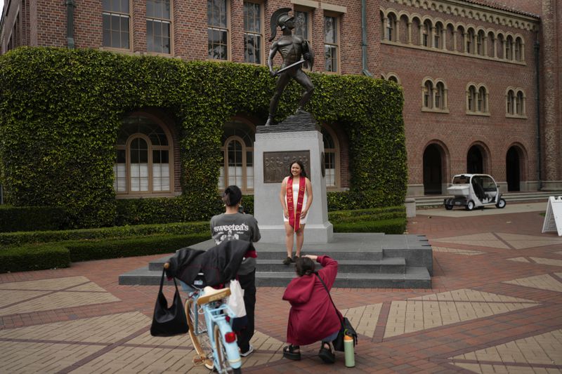 A graduating senior takes photos under the University of Southern California mascot on campus, Thursday, April 25, 2024, in Los Angeles. (AP Photo/Jae C. Hong)