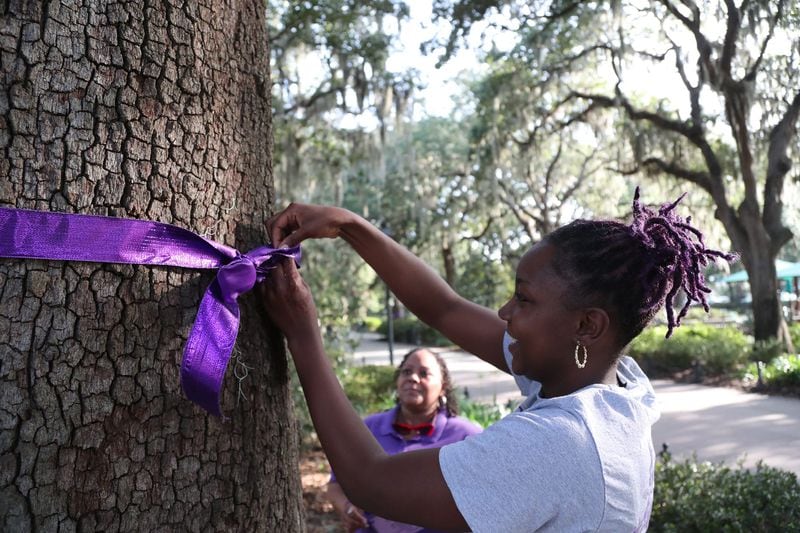 Tajara Muhammad skillfully ties a bow in a purple ribbon wrapped around an oak tree in Forsyth Park on Monday, October 2, 2023 in honor of Domestic Violence Awareness Month. SAFE Shelter will be hosting a candlelight vigil on Thursday October, 5 at 6pm to honor all who've lost their lives to domestic violence in Georgia.
