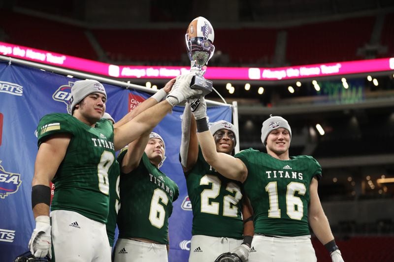 Class AAAA champions: Blessed Trinity players (from left) Jr Bivens (8), Ryan Davis (6), Steele Chambers (22), and JD Bertrand (16) celebrate with the state championship trophy after their 23-9 win against Cartersville at Mercedes-Benz Stadium Wednesday, December 12, 2018, in Atlanta. (Jason Getz/Special)