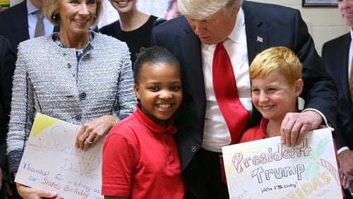 President Donald Trump thanks fourth-graders Janayah Chatelier and Landon Fritz for the homemade greeting cards they presented during his visit to St. Andrew Catholic School in Orlando, Fla., Friday, March 3, 2017. With the president, from left to right, are: Trump son-in-law Jared Kushner; U.S. Secretary of Education Betsy DeVos, and Trump daughter Ivanka Trump. (Joe Burbank/Orlando Sentinel via AP)