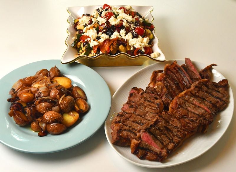 New York strip steaks (right) and Ciambotta Salad (top) are shown here with grilled potatoes and onions (left) as a side dish. (Styling by Pat Pascarella / Chris Hunt for the AJC)
