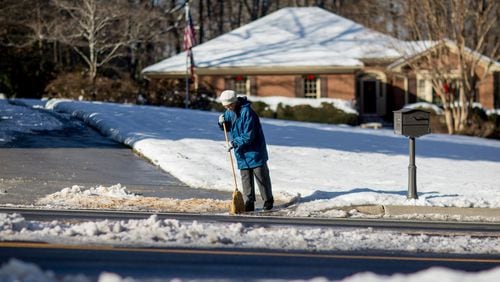 Ice and snow cover parts of Shiloh Road as Kathryn Cavan tries to clear her driveway of ice with a broom, Sunday, Dec. 10, 2017, in Kennesaw, Ga. BRANDEN CAMP