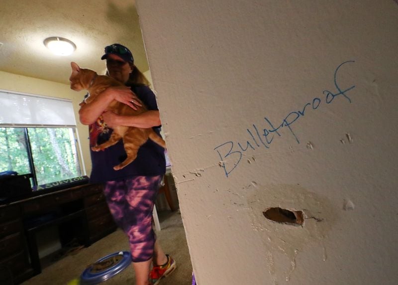 Kristy Neff holds her cat, Judah, next to a bullet hole in the wall of her apartment at The Village at Kensington. She says she wrote "Bulletproof" on the wall after a March incident in which a man fired several shots into her apartment. (Curtis Compton / Curtis.Compton@ajc.com)