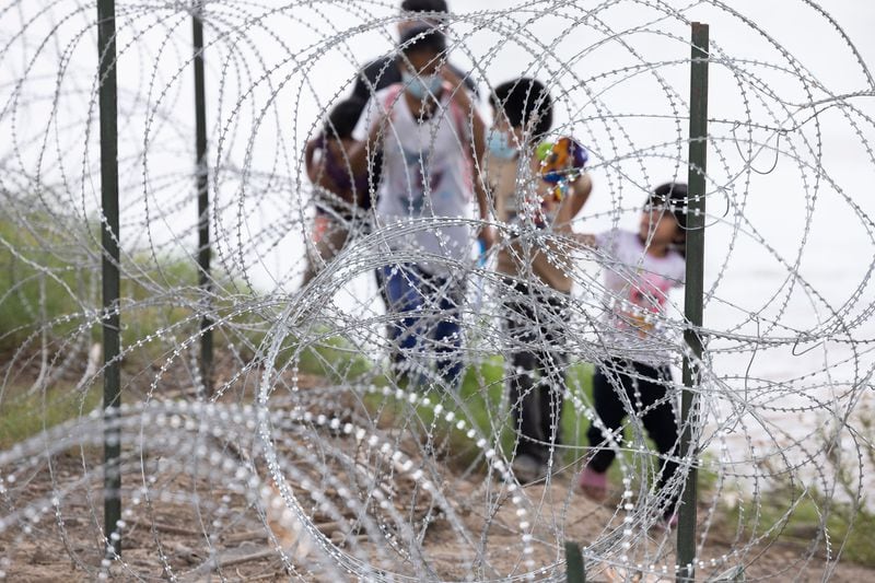 Migrants with children walk by razor wire fencing after crossing the Rio Grande River from Mexico into the U.S. close to the Eagle Pass, Texas. U.S. lawmakers are considering measures to strengthen border control.   (Juan Figueroa/The Dallas Morning News/TNS)