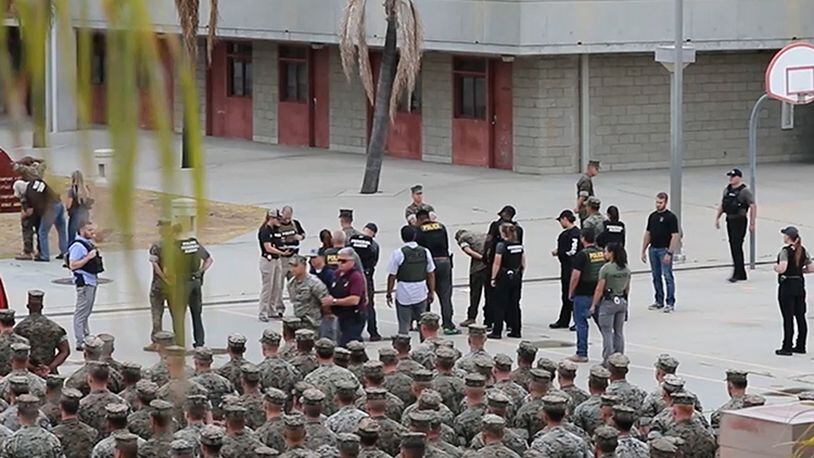 A screenshot shows military law enforcement, including NCIS, handcuff, search and walk detained Marines in front of their peers at Marine Corps Base Camp Pendleton in California.