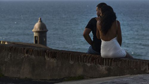 In this Friday, Oct. 20, 2017 photo, a couple watches the sunset from Norzagaray street one month after Hurricane Maria in San Juan, Puerto Rico. The expansive grounds of the Castillo San Felipe del Morro are open around the Spanish fort overlooking San Juan Bay, but the fort itself is still closed. (AP Photo/Carlos Giusti)