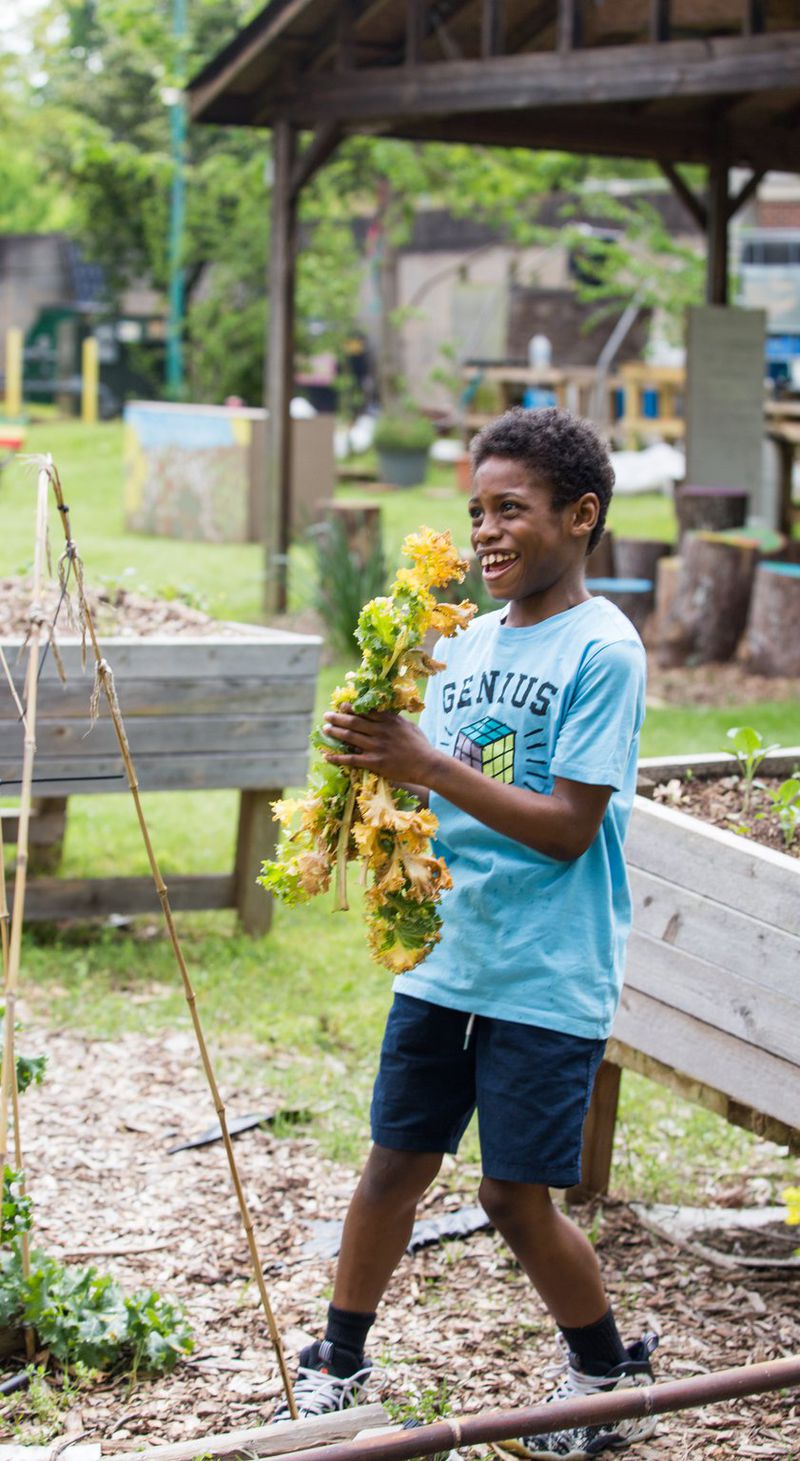 Khaiye Robinson, 11, runs kale clippings to the compost pile to help his mom, Amina Robinson, at the Habesha community garden in the Mechanicsville neighborhood Thursday, April 9, 2020. (Jenni Girtman for Atlanta Journal Constitution)