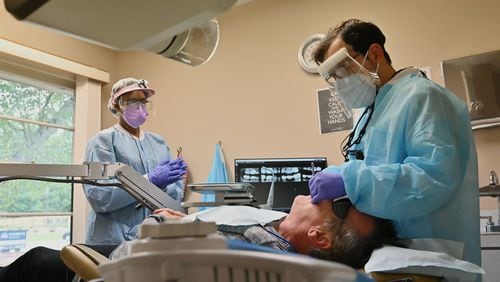 Dr. Daniel Galvez with hygienist Amanda Winn (left) treat a patient at Windy Hill Dentistry. (Hyosub Shin / Hyosub.Shin@ajc.com)