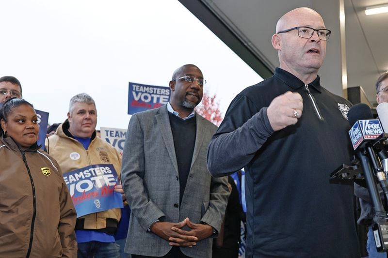 Teamsters general president Sean O’Brien speaks to the media as Sen. Raphael Warnock looks on during a campaign rally at the UPS Smart Hub facility in Atlanta on Monday, December 5, 2022. (Natrice Miller/natrice.miller@ajc.com)  