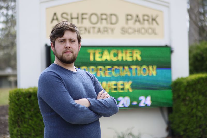 Third-grade teacher Brandon Wyatt poses in front of the school sign at Ashford Park Elementary on Wednesday, March 21, 2023. During his first year of teaching, Wyatt has faced challenges that make his job difficult. "Even though I enjoy teaching the kids, I don't plan to return next year," Wyatt said. (Miguel Martinez /miguel.martinezjimenez@ajc.com.)