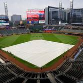Ground crew workers are finishing putting the tarp to cover the diamond at Truist Park as raindrops started to fall moments before the second game of the series between the Atlanta Braves and the New York Mets on Tuesday, April 9, 2024. (Miguel Martinez / miguel.martinezjimenez@ajc.com)