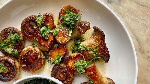 Dark golden brown seared king trumpet and white button mushrooms are topped with zesty lemon gremolata, with an additional bowl of the herby sauce on the side. (Virginia Willis for The Atlanta Journal-Constitution)