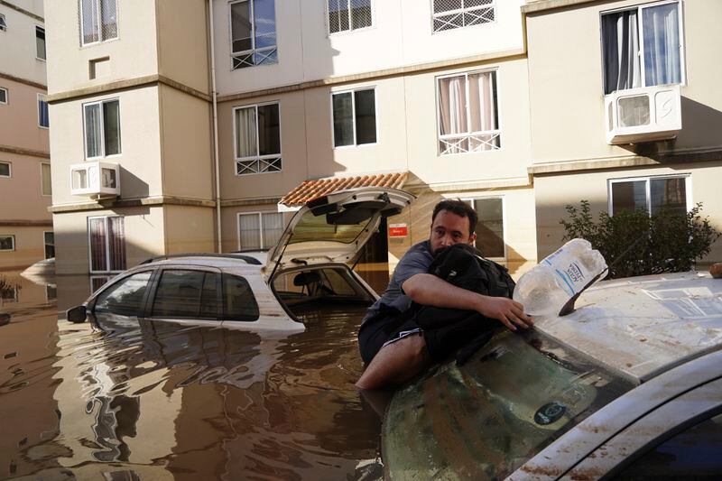 A man supports himself on a car as he tries to return to his flooded apartment building after heavy rain in Canoas, Rio Grande do Sul state, Brazil, Thursday, May 9, 2024. (AP Photo/Carlos Macedo)