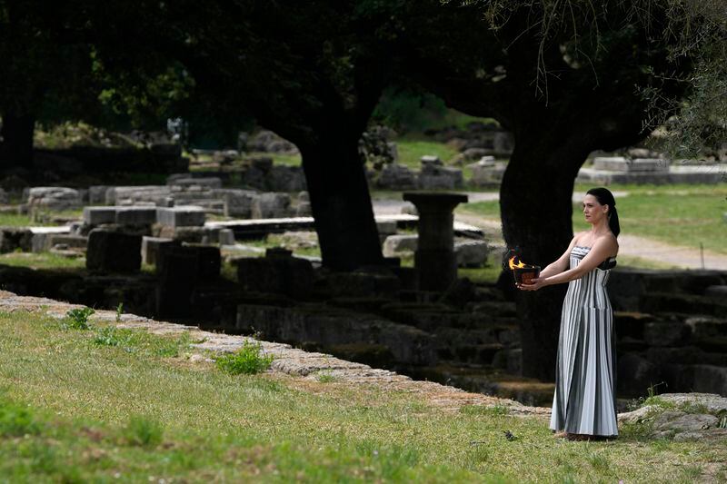 Actress Mary Mina, playing high priestess, carries a ceramic pot with the flame during the official ceremony of the flame lighting for the Paris Olympics, at the Ancient Olympia site, Greece, Tuesday, April 16, 2024. The flame will be carried through Greece for 11 days before being handed over to Paris organizers on April 26. (AP Photo/Thanassis Stavrakis)