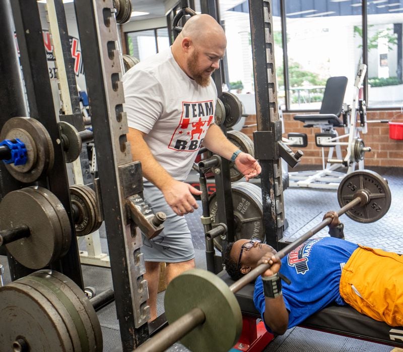 Dave Githutu, a Milton High School weight-lifter who regularly competes in the special olympics, trains at Roswell Barbell with his coach Josh Porter on Tuesday, Aug 23, 2022 and team members.  The athlete is competing in England in September at an able-bodied competition before a scheduled heart surgery scheduled for Spring.  (Jenni Girtman for The Atlanta Journal-Constitution)