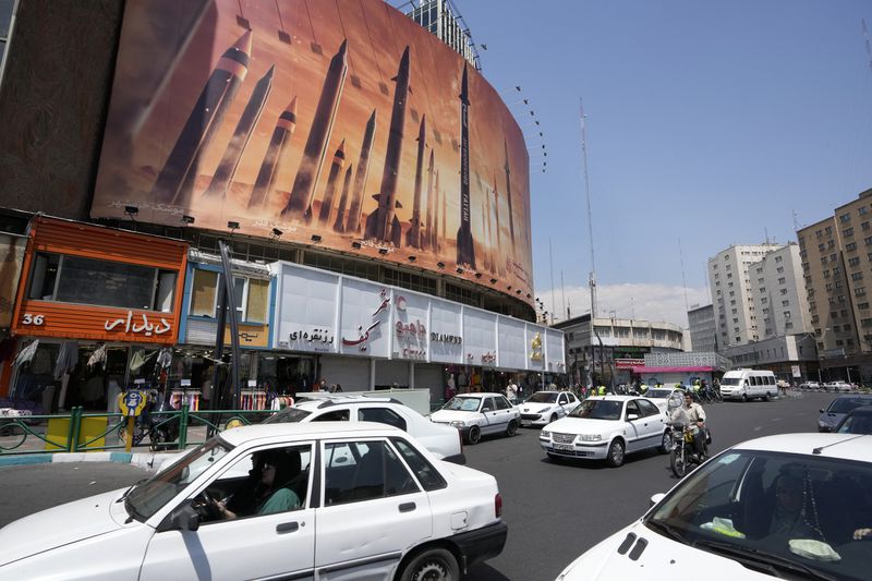 Vehicles drive past an anti-Israeli banner showing missiles being launched, in a square in downtown Tehran, Iran, Friday, April 19, 2024. Iran fired air defenses at a major air base and a nuclear site near the central city of Isfahan after spotting drones early Friday morning, raising fears of a possible Israeli strike in retaliation for Tehran's unprecedented drone-and-missile assault on the country. (AP Photo/Vahid Salemi)