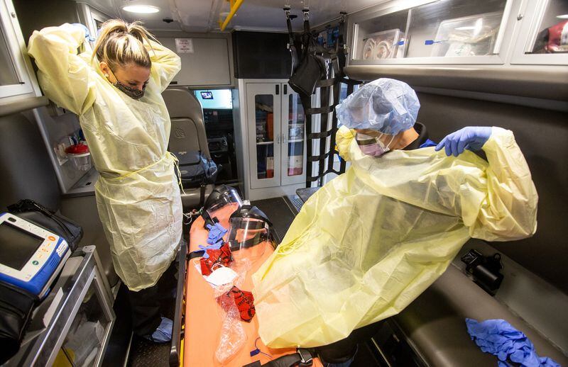 In this file photo taken at the Central EMS office in Roswell, Maci Williams (L), an EMT, and Christopher Kozinski, a paramedic, demonstrate how they put on their personal protective equipment before every call. STEVE SCHAEFER FOR THE ATLANTA JOURNAL-CONSTITUTION