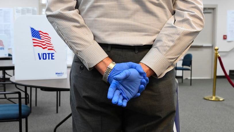 A poll worker wearing protective gloves waits to assist voters during special election voting at city hall to fill an empty city council seat on Tuesday, March 24, 2020, in Dacula. The voting happens to on a day that was supposed to be the test run for the state's new election system before coronavirus COVID-19 caused it to be called off.