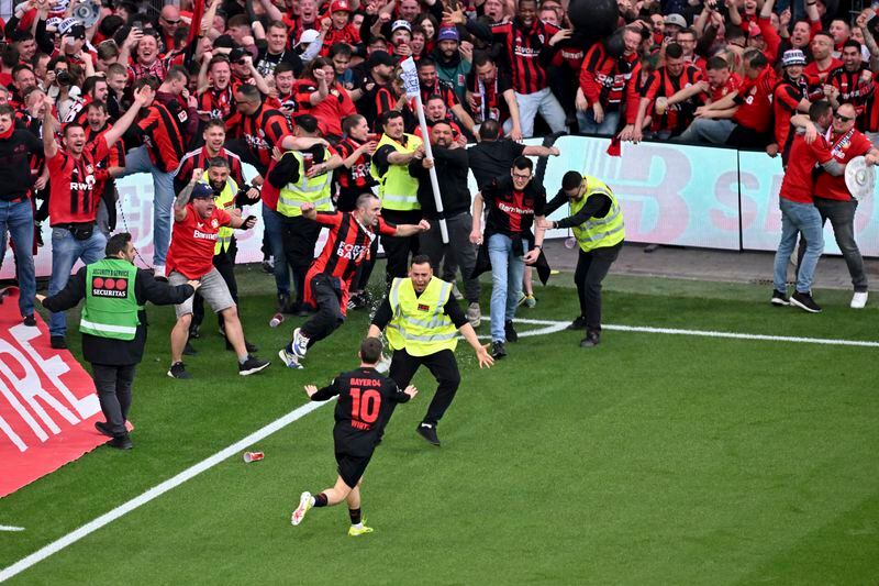 Leverkusen's Florian Wirtz calms down fans and security personnel as he celebrates after scoring his side's fourth goal of the game during the Bundesliga soccer match between Bayer Leverkusen and Werder Bremen at the BayArena in Leverkusen, Germany, Sunday April 14, 2024. (David Inderlied/dpa via AP)