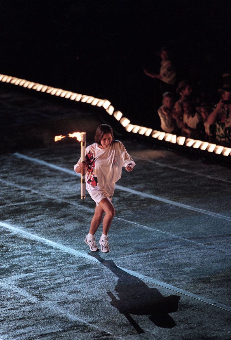 Swimmer Janet Evans carries the flame up the ramp to pass to Muhammad Ali during the Opening Ceremonies. (Cox Staff Photo/Allen Eyestone)