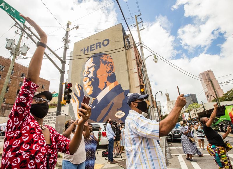 Rep. John Lewis' casket and motorcade pauses along Auburn Ave near Jesse Hill Jr Drive in front of the Hero mural where Karren Grant, of Peachtree Corners, left, pays respect to the Congressman and his family on Wednesday, July 29, 2020.  (Jenni Girtman for The Atlanta Journal-Constitution)