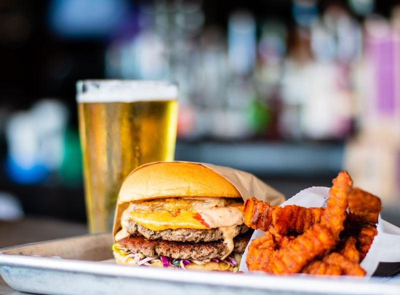 The meat-substitute Impossible Burger, Dixie Style, with sweet potato fries and a beer at Grindhouse Kiiller Burgers on Memorial Drive. Dixie Style means it comes with pimento cheese, fried green tomato, Carolina coleslaw, and chipotle ranch. CONTRIBUTED BY HENRI HOLLIS