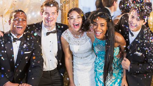 A group of five multi-ethnic teenagers and young adults dressed in formalwear - dresses and tuxedos.
